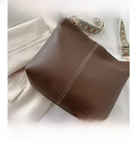 Detail of brown leather bucket bag with white stitching and colorful woven strap