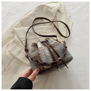 Détail d'un sac seau à carreaux en tissu laineux avec une poignée en cuir tressé