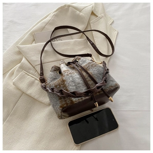 Détail de l'anse en cuir tressé et des ferrures dorées sur le sac seau à carreaux