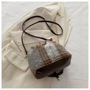 Détail du sac seau à carreaux en peluche avec base en cuir sur un costume beige