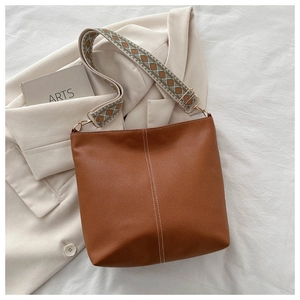 Detail view of brown bucket bag with geometric woven strap and white stitching