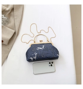 Detail view of retro forest print bag with metal clasp and chain next to a smartphone