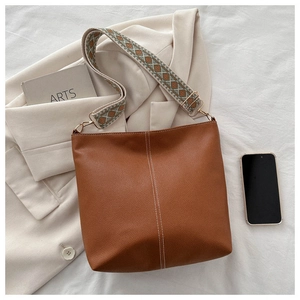 Detail of brown leather bucket bag with geometric strap and white stitching accents