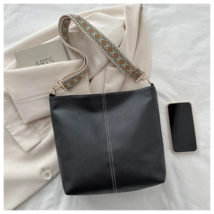 Detail of black lychee texture bucket bag with contrast stitching and ethnic woven strap
