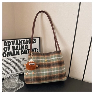 Close-up of green and brown plaid tote bag with gold flower buckle and fuzzy charm