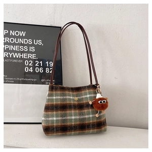 Detail of plaid wool tote bag featuring a green checkered pattern and brown plush pendant