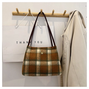 Detail of vintage plaid wool tote bag with golden flower buckle on a wooden hanger