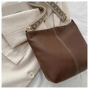 Detail of dark brown leather bucket bag featuring white stitching and ethnic fabric strap