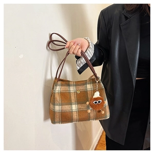 Detailed shot of brown plaid tote bag with golden flower logo and plush monster charm