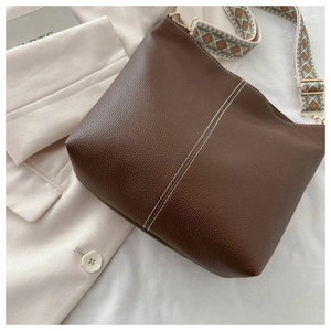 Detail of brown litchi pattern leather bag with white stitching and jacquard strap