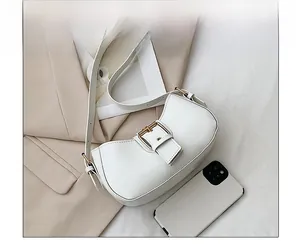 Detailed view of a white semi-moon shoulder bag with a metal buckle next to a phone