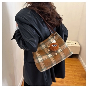 Brown tartan tote bag with plush monster charm worn by model in black leather jacket