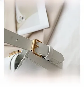 Close-up of golden metal buckle and stitching on white leather minimalist handbag