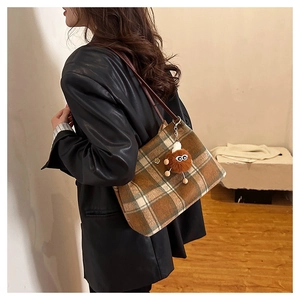 Detail view of a plaid woolen tote bag with a plush monster charm on a female model