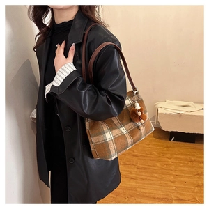 Detail of wool plaid tote bag featuring brown checkered pattern and plush pompom charm