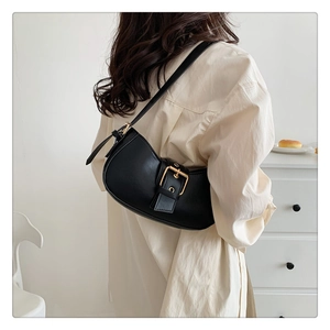 Detail of black faux leather crescent shoulder bag with golden buckle on white shirt