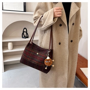Detail of red and green plaid woolen tote bag with brown leather strap and charm