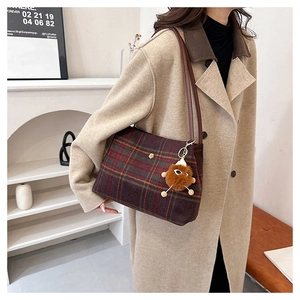 Macro detail of retro plaid tote bag with golden floral badge and brown plush charm