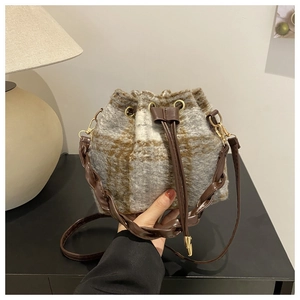 Détail d'un sac seau à carreaux avec poignée en cuir tressé et fermeture à cordon