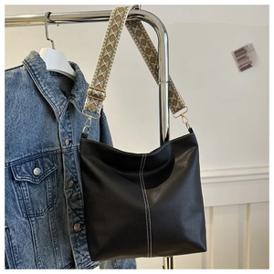 Detail of black textured hobo bag featuring white stitching and geometric wide strap