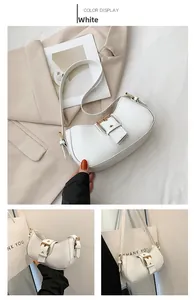 Detail view of white crescent bag with golden buckle and adjustable strap on beige blazer