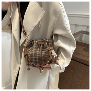 Détail d'un sac seau à carreaux avec poignée tressée et accessoire de charme en peluche