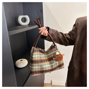 Detail of tweed plaid tote bag showing texture, leather handles and plush charm accessory