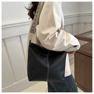 Detail of black bucket bag with white stitching and embroidered wide strap on model