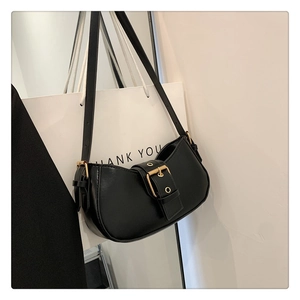 Detailed view of black leather saddle bag with large golden buckle and adjustable strap