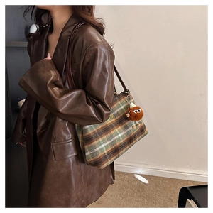 Close-up of green plaid wool tote bag with a brown plush charm and leather strap