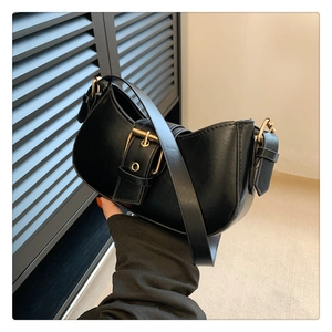 Detail of black leather half-moon shoulder bag featuring a prominent gold buckle hardware