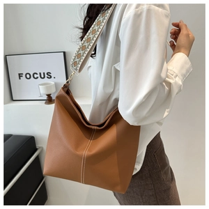 Detail of a brown leather tote bag with white stitching and colorful ethnic strap