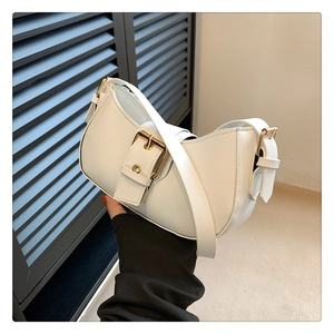 Detail of white half-moon shoulder bag with a prominent golden square buckle and leather strap