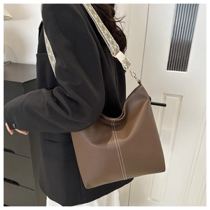 Macro detail of brown leather bucket bag featuring white stitching and ethnic woven strap
