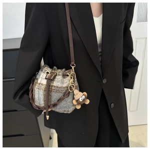 Détail du sac seau à carreaux avec breloque ours en peluche et bandoulière en cuir