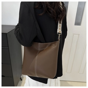 Brown bucket bag with white contrast stitching and wide jacquard geometric strap