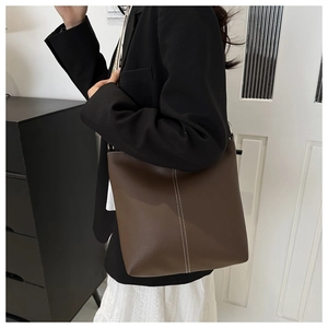 Detail view of dark brown pebbled leather tote bag with vertical white contrast stitching