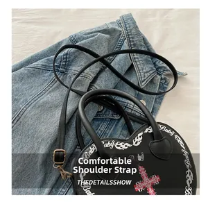 Detail of the slim black leather strap on a gothic heart-shaped printed crossbody bag