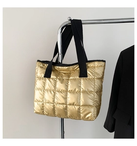 Detail view of gold quilted puffer tote bag with black strap and textured stitching