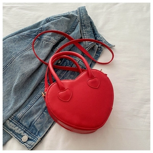 Flat lay of a red heart-shaped PU leather bag with top handles on a denim jacket