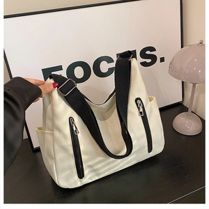 Détail d'un sac cabas en toile montrant des sangles noires et des fermetures éclair