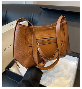Detail view of brown pebbled leather shoulder bag with gold chain and front zip pocket