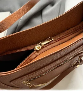 Detail view of the smooth golden metal zipper on a brown pebble grain leather shoulder bag