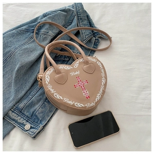 Detail of heart-shaped beige crossbody bag with white prints and red cross accent
