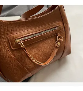 Close-up of brown textured leather shoulder bag with gold zipper and chain detail