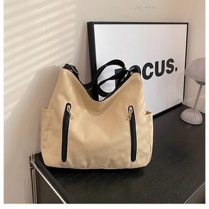 Détail du sac hobo en toile beige avec deux poches zippées noires et finitions dorées