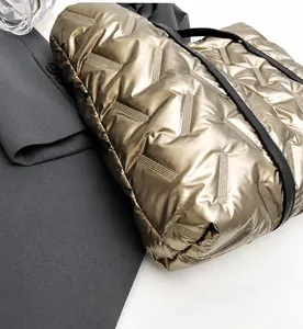 Detail of quilted metallic tote bag with diagonal stitching and black handles