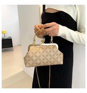 Dettaglio borsa vintage beige con chiusura a cuore dorata e motivi geometrici a trifoglio