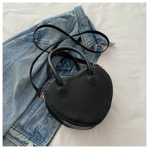 Close-up of heart-shaped black leather handbag with crossbody strap on denim jacket