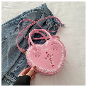 Detail shot of a pink heart-shaped bag with white Baby lettering and vintage cross print